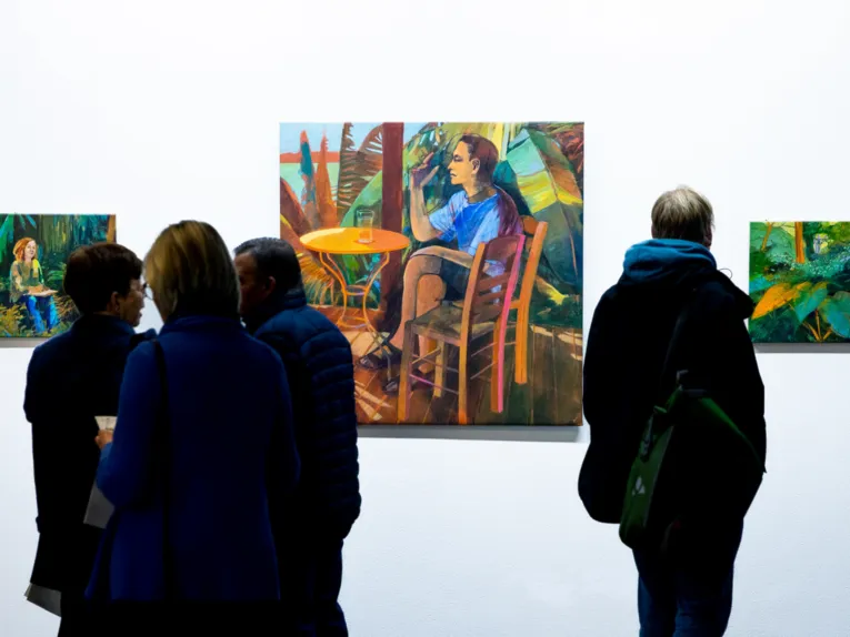 Publikum blickt auf Werke im Regionshaus, Schauplatz f&uuml;r Kunst. Die Bilder zeigen Menschen in farbenfroher tropischer Natur.