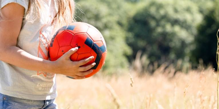 Ein Kind hält einen roten Fußball mit beiden Händen.