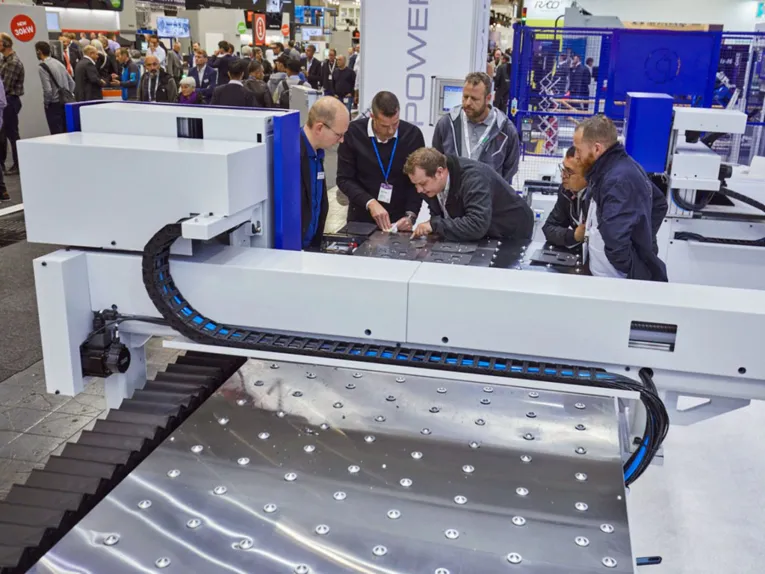 Ein Mann erklärt anderen Männer etwas vor einer großen Maschine mit Metallplatten.