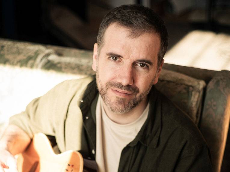 Mann mit kurzem Haar und Bart und Gitarre