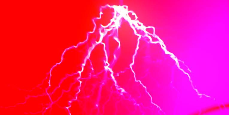 Blitze zucken bei einem physikalischen Experiment in einem roten Raum von der Decke.