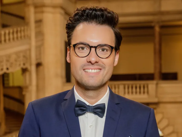 Eine Person im Anzug und mit einer Brille mit schwarzem rand schaut in die Kamera.