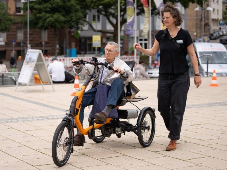 Ein älterer Herr auf einem Spezialfahrrad. Daneben eine Frau, die alles erklärt.