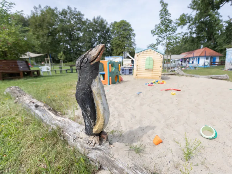 Im Vordergrund geschnitzter Pinguin, Sandkiste mit Spielhaus und Kletterm&ouml;glichkeit