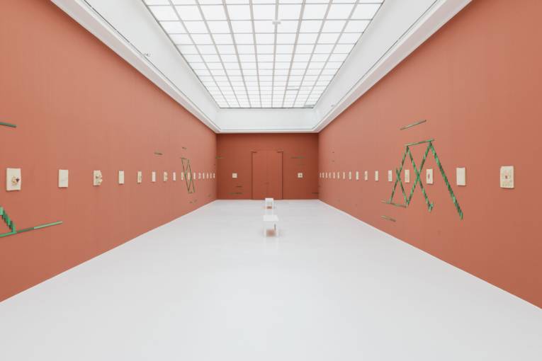 Ein Stuhl in einem Ausstellungsraum, an dessen Wände Kunst hängt und klebt