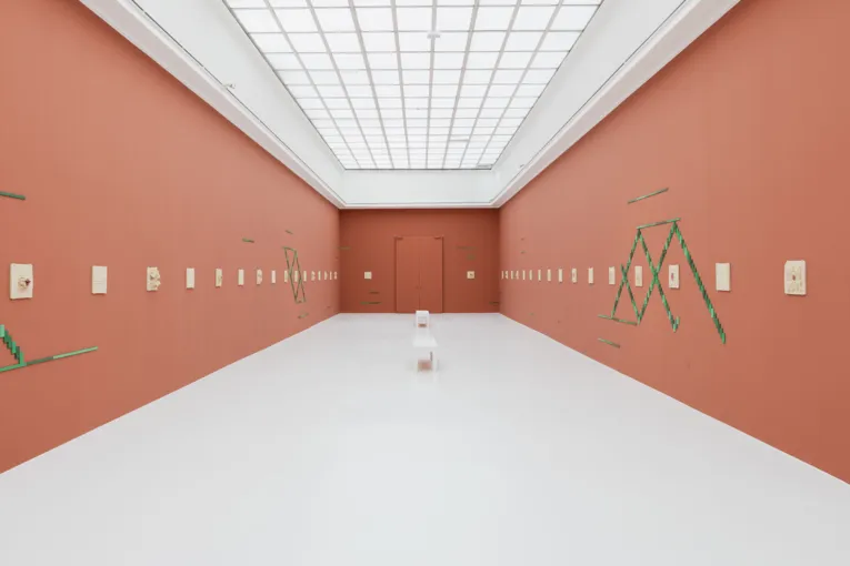 Ein Stuhl in einem Ausstellungsraum, an dessen Wände Kunst hängt und klebt