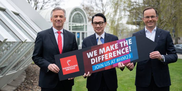 Drei Männer in Anzügen halten ein Plakat.