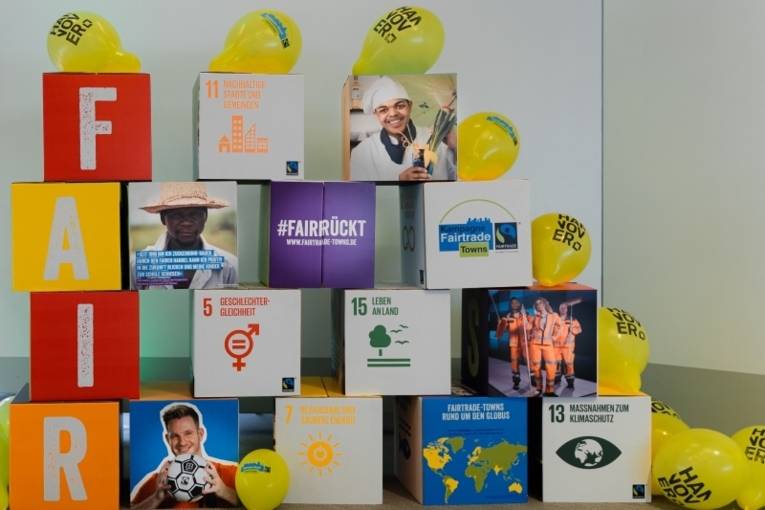Pappwürfel mit Fotos und Symbolen der SDGs und den Buchstaben "Fair". Drumherum Luftballons mit dem Hannover-Logo.