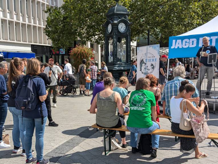 Personen stehen am Kröpcke vor einem Podest, auf dem ein Redner spricht.