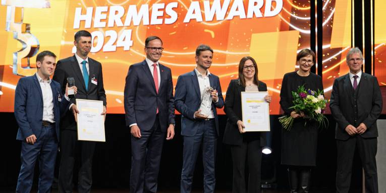 Zwei Frauen und fünf Männer mit Urkunden, Blumen und Gegenständen in den Händen, im Hintergrund steht "Hermes Award 2024"