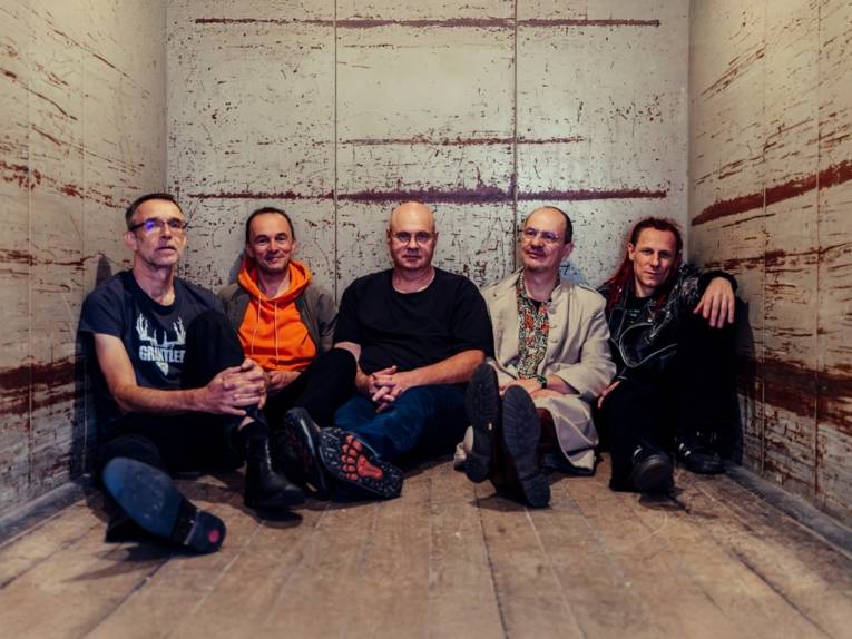 Zu sehen ist die Band „Brutal verschimmelt“. Die Bandmitglieder sitzen auf dem Boden.