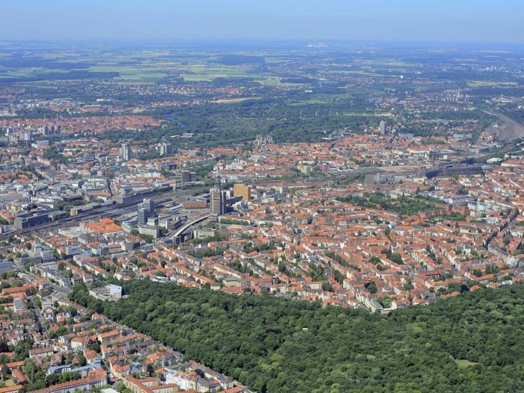 Innenstadt und Stadtwald Eilenriede liegen beieinander, Wohnhäuser, Geschäftsgebäude, Bahngleise und der Hauptbahnhof Hannover sind zu erkennen.