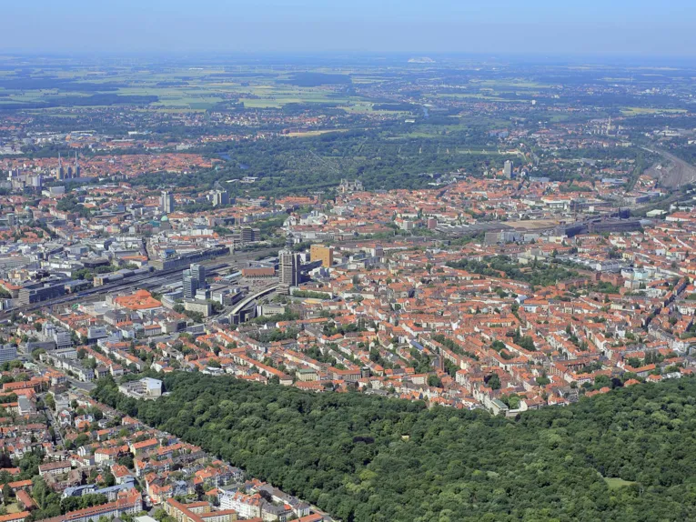 Innenstadt und Stadtwald Eilenriede liegen beieinander, Wohnhäuser, Geschäftsgebäude, Bahngleise und der Hauptbahnhof Hannover sind zu erkennen.