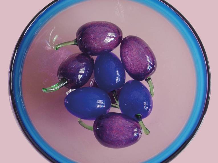 Zu sehen ist eine Glasschale in der Trauben, ebenfalls aus buntem Glas, liegen.