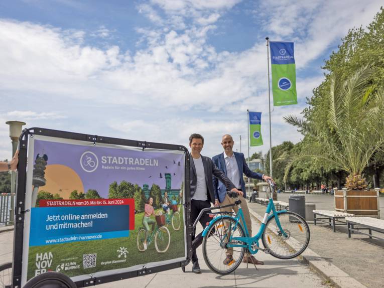 Zwei Herren mit einem Fahrrad und einem Werbebanner fürs Stadtradeln 2024.