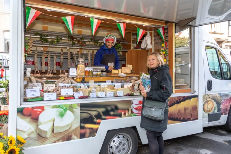 Ein Verk&auml;ufer bietet einer Kundin italienische Wurst- und K&auml;sewaren an.