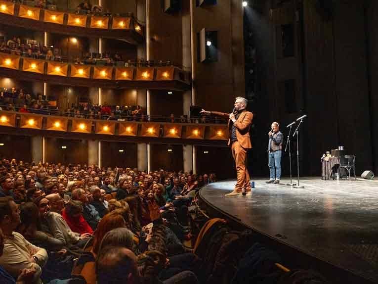 Zwei Männer stehen auf einer Bühne und reden zum Publikum