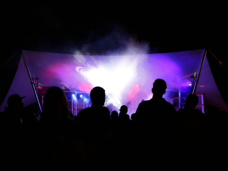 Publikum ist als Schatten erkennbar, das Publikum verfolgt ein Konzert auf einer hell leuchtenden Bühne.