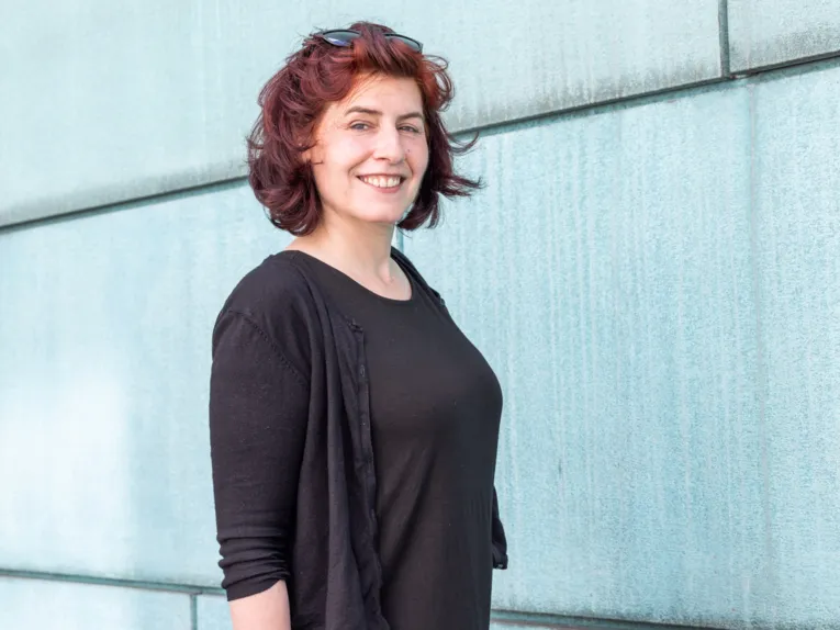 Portr&auml;tfoto einer Frau vor einer t&uuml;rkisfarbenen Fassade.