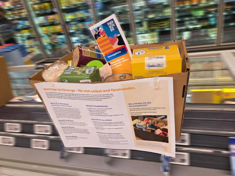 Ein Karton mit Lebensmittelpackungen steht in einem Supermarkt auf einer Kühltruhe.