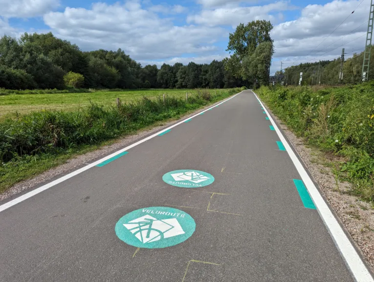 Ein asphaltierter Weg, links Wiese und Bäume, rechts eine Bahntrasse.