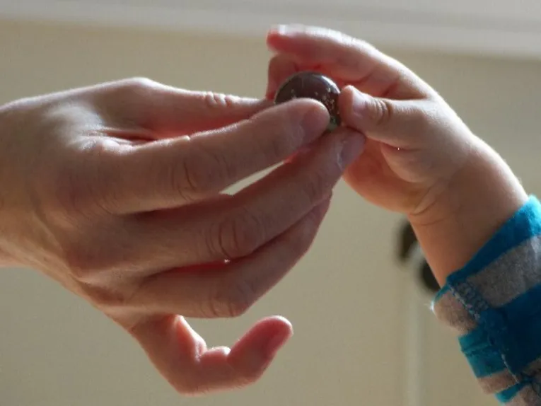 Eine Erwachsenen- und eine Kinderhand, die eine Murmel halten.