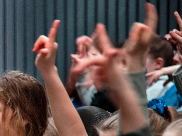 Kinder heben ihre Arme und Finger und signalisieren dadurch, dass sie etwas beitragen oder eine Frage stellen wollen.
