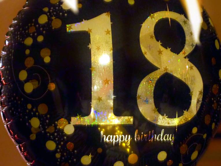 Auf einem dunklen Ballon ist eine goldene 18 und darunter in kleiner Schrift "happy birthday".