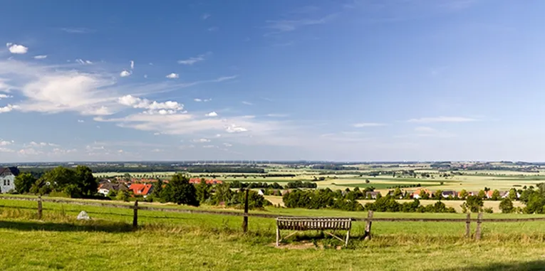 Eine Bank lädt vor einer Viehweide zur Rast ein. In der Ferne zeichnet sich der Deister vor blauem Himmel ab.