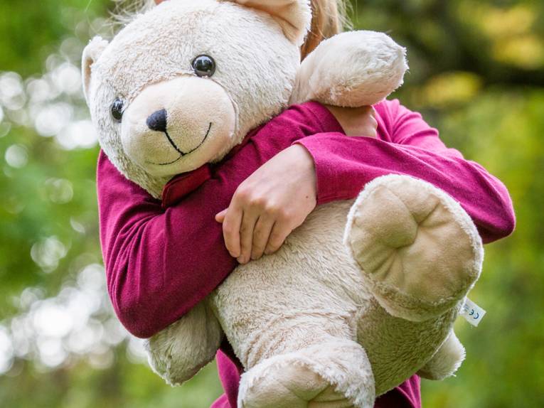 Ein Kind hält einen großen Teddybären vor der Brust.
