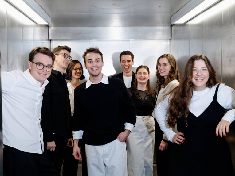 Die jeweils vier jungen Sängerinnen und Sänger des Ensembles stehen in einem Fahrstuhl.
