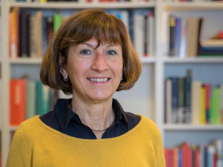 Portraitfotografie einer Frau mit einem verschwommenen Bücherregal im Hintergrund.