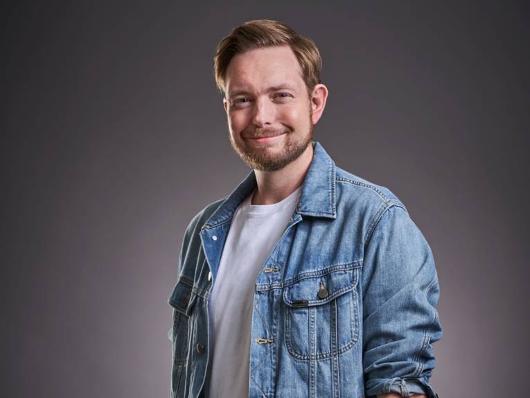 Zu sehen ist ein junger Mann mit Bart in einer Jeansjacke.