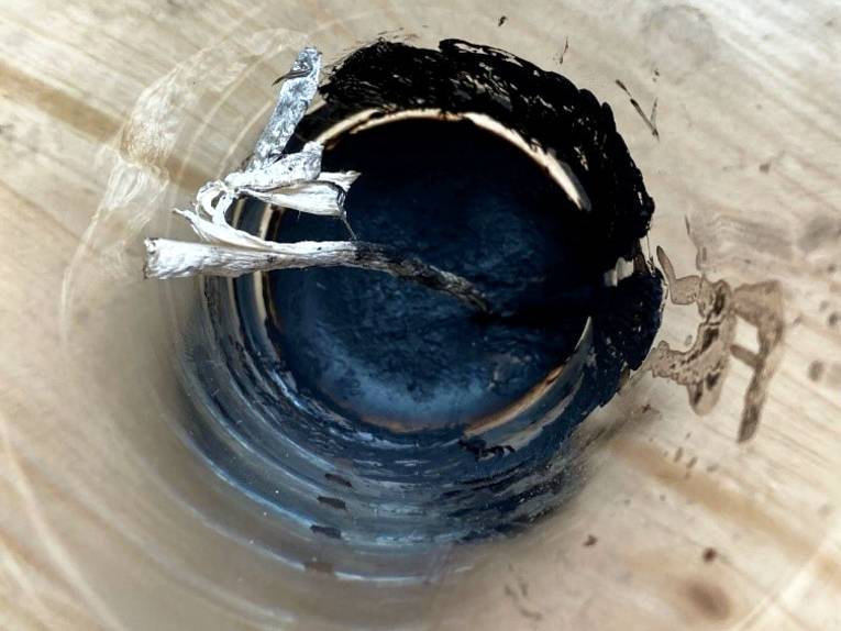 Die Reste eines Pilz sind in einem Glas getrocknet, eine schwarze Substanz hat sich auf dem Glasboden gesammelt.