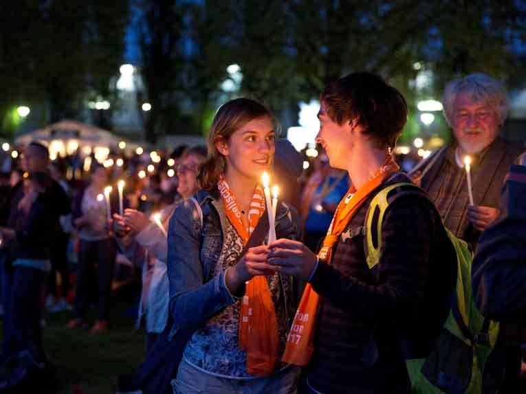 Ein junges, heterosexuelles Pärchen hält zwei brennende Kerzen in den Händen und blickt sich tief in die Augen
