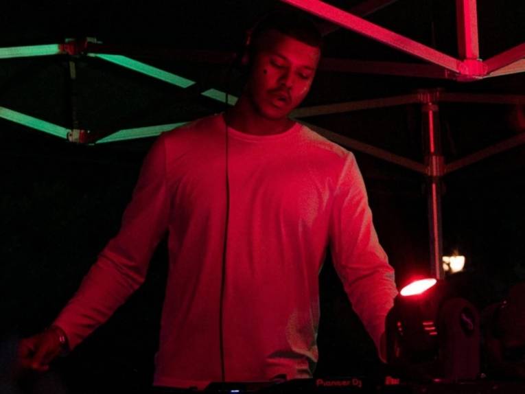 Mann steht an einem Mischpult und hat Kopfhörer auf. Neben ihm ist ein Scheinwerfer, der rotes Licht ausstrahlt.