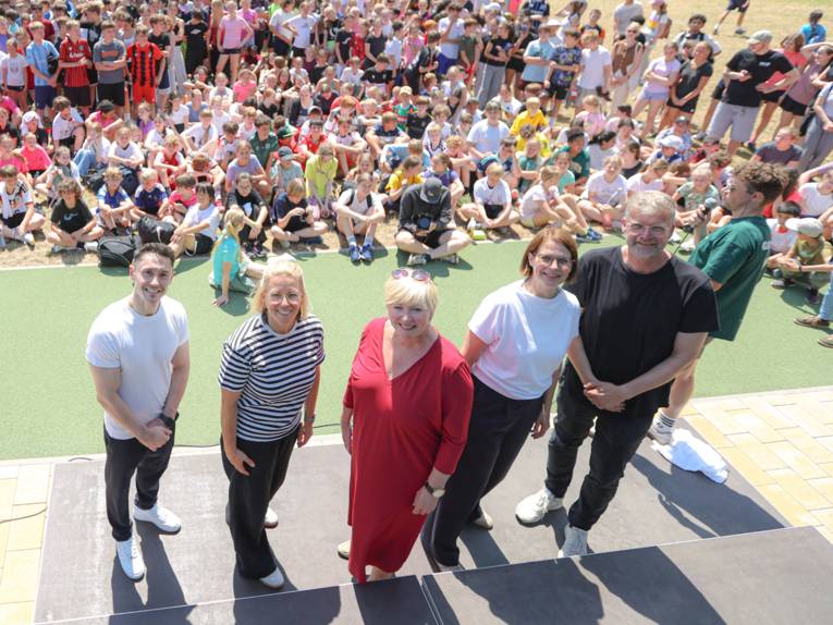 Vier Personen auf einer Bühne. Im Hintergrund sehr viele Kinder.