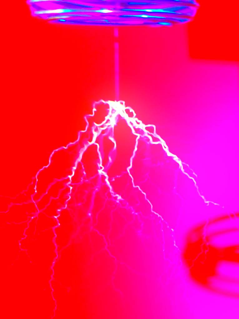 Blitze zucken bei einem physikalischen Experiment in einem roten Raum von der Decke.