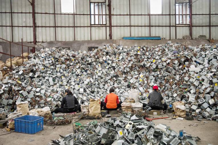 Drei Menschen sitzen vor einer großen Menge Elektroschrott, den sie bearbeiten.