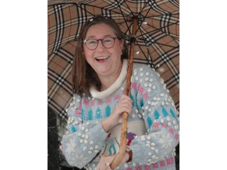 Eine lachende Frau in einem Strickpulli mit winterlichem Motiv und Regenschirm im Schnee.