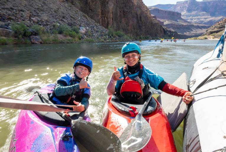 Zwei Jungs im Kajak halten sich an einem Schlauchboot fest