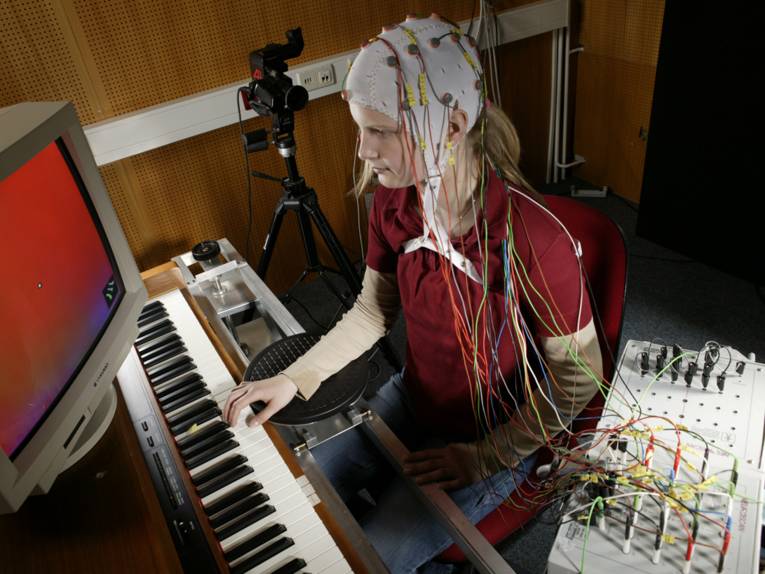 Ein Mädchen spielt Klavier während an ihrem Kopf Sensoren befestigt sind.