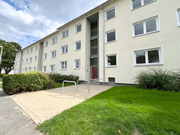 Dreigeschossige Wohnh&auml;user mit gelber Fassade, davor Fahrradb&uuml;gel auf den Zuwegungen, daneben gr&uuml;ner Rasen und eine Hecke.