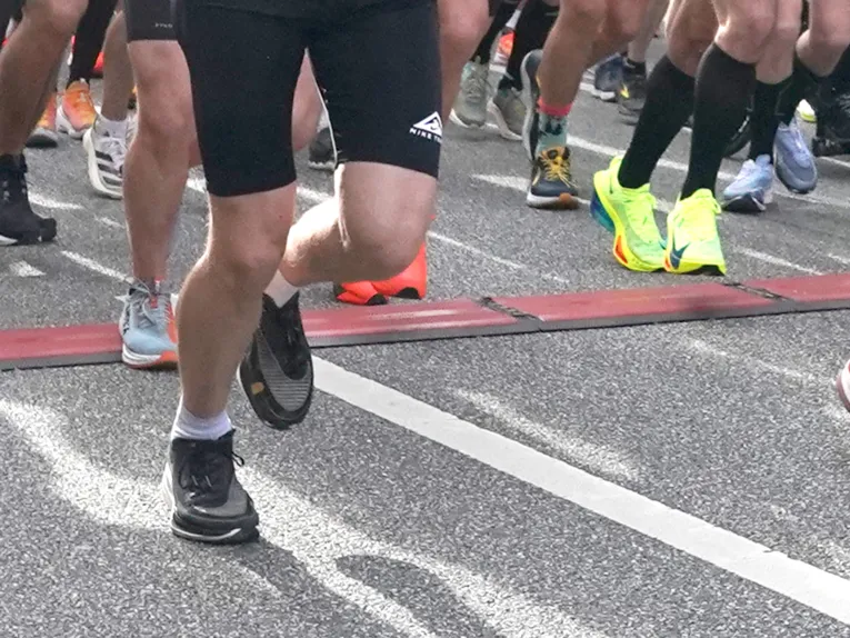Ausschnitt von Menschen, die auf Asphalt in Sportsachen und Laufschuhen laufen, zu sehen sind die Beine und Füße.