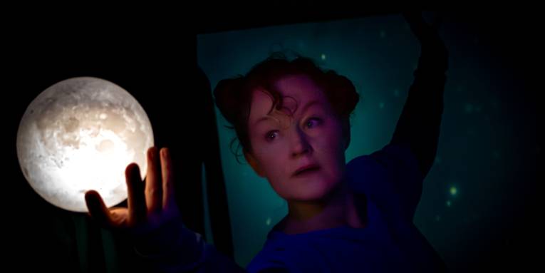 Theaterszene: Eine Frau schaut auf ihre Hand und den Mond in ihrer Hand.