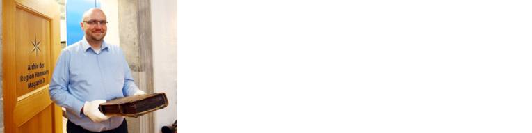 Ein Mann mit wei&szlig;en Handschuhen an, mit denen er einen Folianten h&auml;lt.