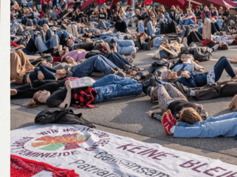 Zu sehen ist eine Protestaktion auf der Straße, auf der Menschen auf dem Boden liegen.