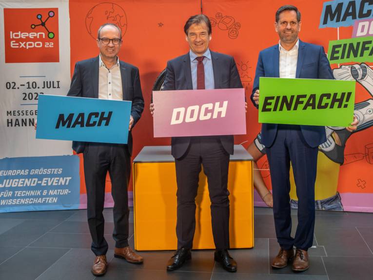 Drei Männer halten Schilder mit den Wörtern "Mach", "doch" und "einfach".