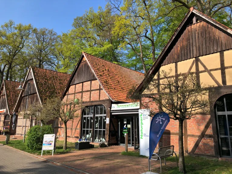 Mehrere historische Fachwerkscheunen stehen nebeneinander. Zwischen zwei Scheunen ist eine Glast&uuml;r, dar&uuml;ber ein Banner mit dem Text: "INFOZENTRUM". In der N&auml;he der Eingangst&uuml;r sind noch weitere Aufsteller, Displays etc. mit dem Logo des Naturparks Steinhuder Meer oder der Region Hannover.