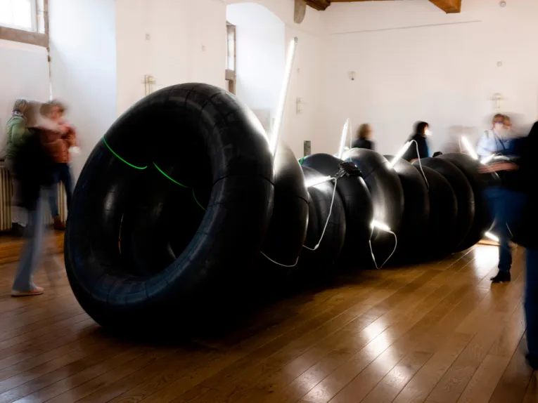 Schwarze Gummireifen und Leuchtschl&auml;uche bilden eine Kunstinstallation. Besucherinnen und Besucher dieser Ausstellung im Schloss Landestrost sind durch ihre Bewegungen unscharf zu erkennen.